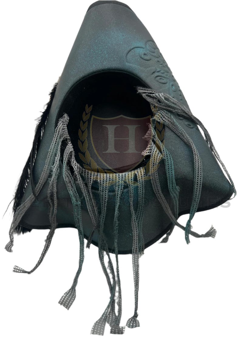 Puede incluir: Un sombrero de tres picos en color verde azulado oscuro con acabado desgastado, detalles de plumas negras y tiras de malla gris colgantes. El interior muestra un emblema circular con una letra H rodeada por una corona de laurel dorada.
