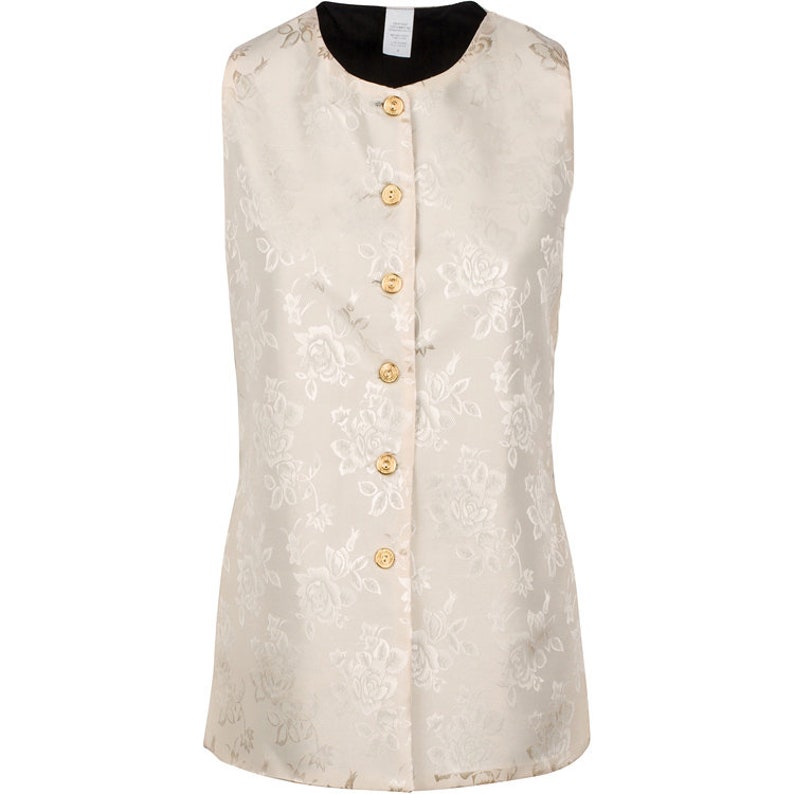 May include: A sleeveless vest in a cream-colored fabric featuring a tonal floral jacquard pattern. The garment has a round neckline, a black interior lining, and a front closure secured by six round, gold-toned buttons with a textured surface.