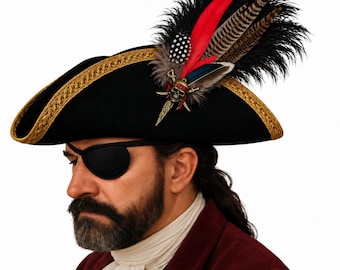 May include: A black pirate hat featuring gold braided trim along the edges, adorned with a cluster of black, red, and patterned feathers. A metallic skull and crossbones emblem with a small dagger detail is attached to the side of the hat.