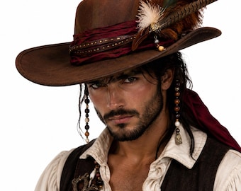 May include: A brown wide-brimmed hat featuring a dark red fabric band with metallic studs, adorned with a cluster of brown and green feathers. The hat is accented with a decorative gold-toned metal piece and hanging beaded strands on the sides.
