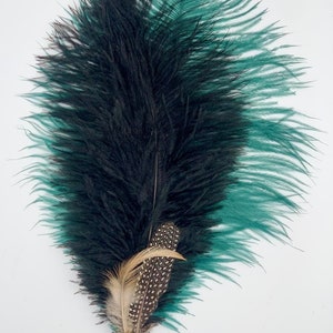 Op de afbeelding: Een zwarte en turquoise struisvogelveer met een gouden decoratief accent. De veer is lang en vloeiend, met een delicate textuur.
