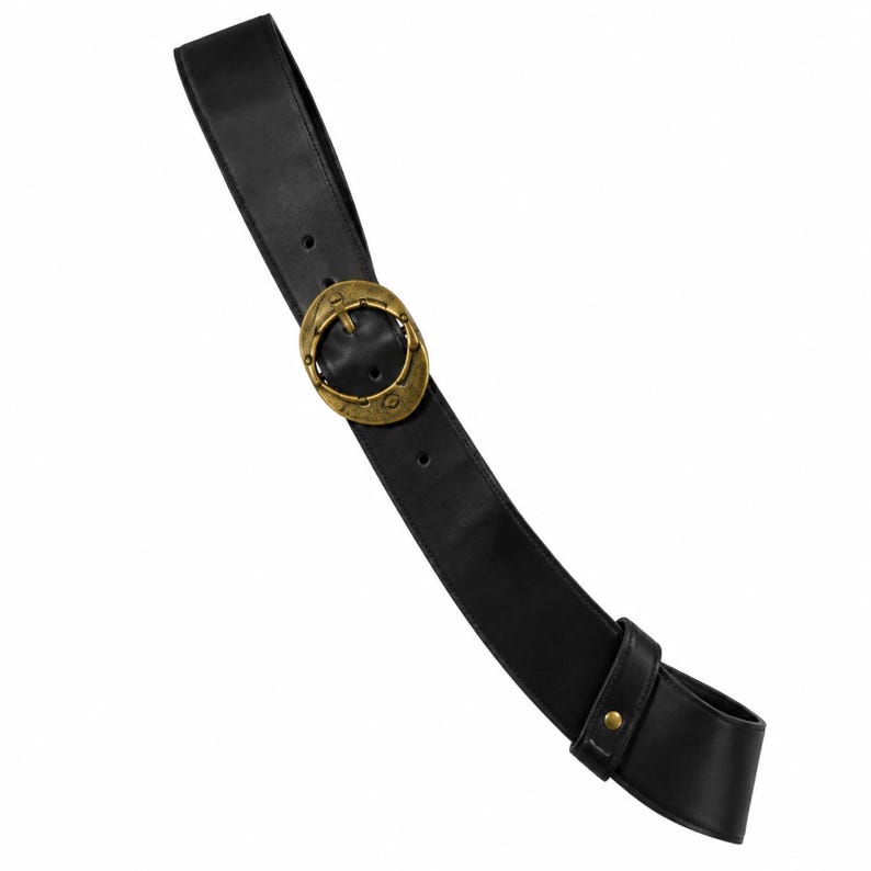 May include: A black belt featuring a wide strap and a large, circular, antique brass-toned metal buckle. The buckle has a textured, weathered finish with a central pin. A matching black leather loop secures the end of the belt strap.