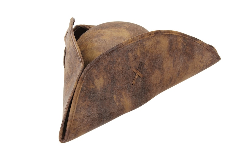 May include: A brown tricorn hat with a distressed, weathered texture. The hat features a rounded crown and a wide, upturned brim that is folded into a triangular shape. A small, stitched X-shaped detail is visible on the side of the brim.
