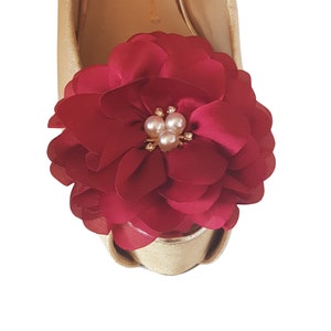 Puede incluir: Primer plano de un broche de zapato de flor burdeos con un adorno de perlas y oro.