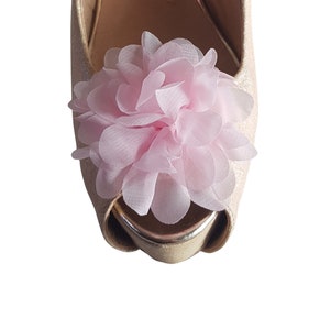 Könnte beinhalten: Ein Paar goldene Glitzer-High-Heels mit einer rosa Blumenverzierung.