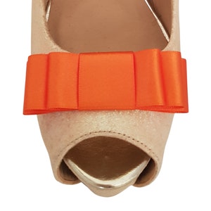 May include: A pair of beige peep-toe heels with a bright orange satin bow on the top.