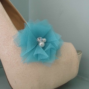 Puede incluir: Un par de tacones altos blancos con purpurina con una flor de tul turquesa y detalles de perlas.