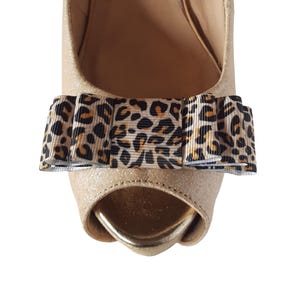 May include: Gold peep-toe heels with a leopard print bow on the front.