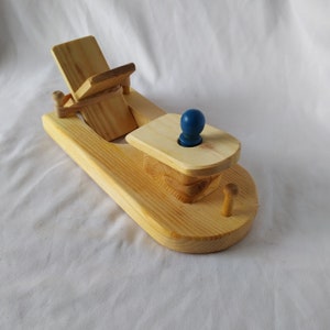May include: A wooden toy boat with a blue knob for a captain. The boat has a hinged seat that can be raised and lowered.