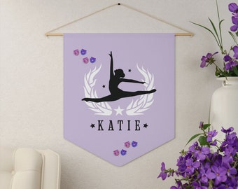 May include: A purple banner with a silhouette of a gymnast in a split pose. The banner has a white laurel wreath with stars around the gymnast. The banner also has the name "KATIE" printed in black letters.