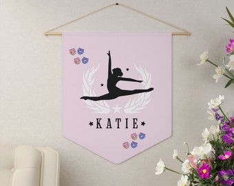 May include: Pink fabric banner with a silhouette of a dancer in a split position. The banner has white laurel wreaths and stars. The name "KATIE" is printed in black below the dancer.