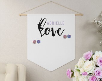 May include: White banner with a black silhouette of a gymnast holding a hoop. The banner has the text "Abrielle Love" in black cursive lettering. There are three small colorful pins on the banner.