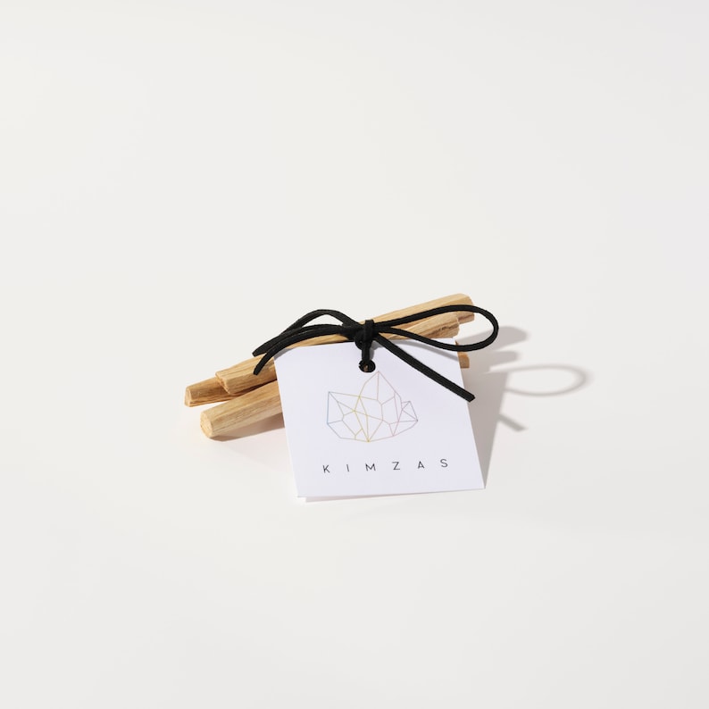 May include: A bundle of Palo Santo sticks tied with a black ribbon and a white tag that says "KIMZAS" with a geometric crystal design.
