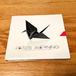 May include: A square music CD case with a white cover featuring a black origami crane graphic with a small red dot. The text FATES WARNING and DARKNESS IN A DIFFERENT LIGHT is printed in black below the crane, with a red triangle on the right edge.