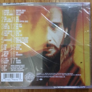 May include: The back of a CD case with a close-up of a man's face. The case is yellow and red with a list of song titles and track numbers. The text on the case reads "Unauthorized copying is punishable under federal law."