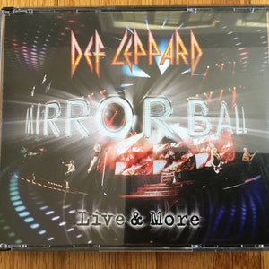 May include: A CD case with a black background and a silver and red image of the band Def Leppard. The text "Mirror Ball Live & More" is printed in white on the case.