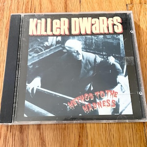 May include: A CD case featuring the album "Method to the Madness" by Killer Dwarfs. The album cover has a black and white image of a person in a dark setting, with the band's name in red and white text at the top.