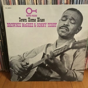May include: A vintage vinyl record album cover featuring a black and white photo of a man playing a guitar. The album title is "Down Home Blues" by "Brownie McGhee & Sonny Terry".