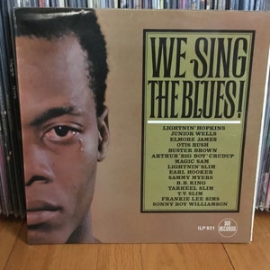 May include: A vintage vinyl record album cover featuring a black and white photo of a man with a tear rolling down his cheek. The album title is "We Sing The Blues!" and lists the artists: Lightnin' Hopkins, Junior Wells, Elmore James, Otis Rush, Buster Brown, Arthur 'Big Boy' Crudup, Magic Sam, Lightnin' Slim, Earl Hooker, Sammy Myers, B.B. King, Tarheel Slim, T.V. Slim, Frankie Lee Sims, and Sonny Boy Williamson. The album is on Sue Records and has the catalog number ILP 921.