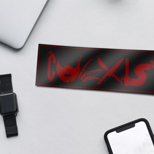 May include: Black and red sticker with the word "COEXIST" in red letters. The letters are made up of various horror movie weapons, including a hockey mask, a knife, and an axe.
