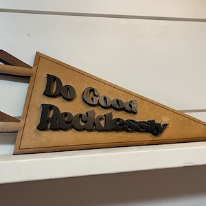 Puede incluir: Un banderín de madera con el texto "Do Good Recklessly" en letras negras.