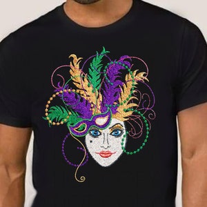 May include: A black t-shirt with a colorful Mardi Gras mask design. The mask is purple, green, and gold with feathers and beads.
