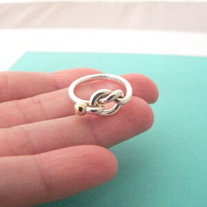 May include: A silver ring with a twisted knot design and a small gold bead accent.