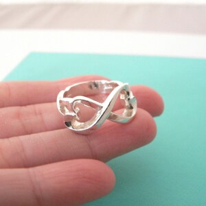 May include: A silver ring with an infinity symbol design featuring two intertwined hearts.
