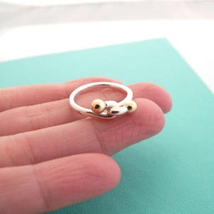 May include: A silver ring with two gold balls on the band.