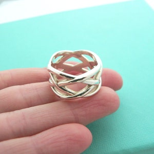 May include: A silver ring with a woven design. The ring is thick and has a wide band.