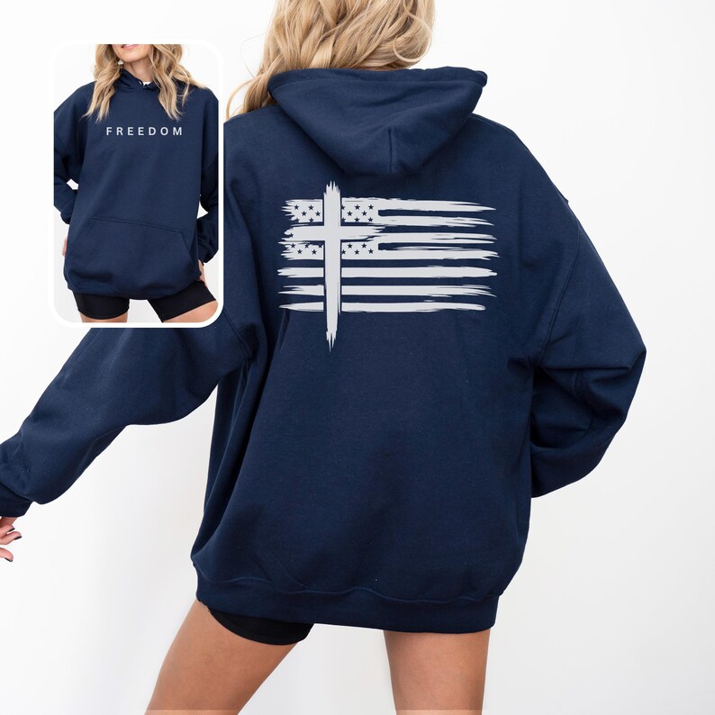 Op de afbeelding: Marineblauwe hoodie met een wit kruis- en vlagontwerp op de rug. Het woord "FREEDOM" is op de voorkant gedrukt. De hoodie heeft een capuchon en een voorzak. Het ontwerp is in een distressed, borstelstijl.