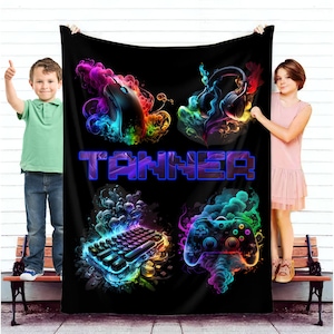 May include: A black fleece blanket with a colorful gamer theme. The blanket features a mouse, headphones, a keyboard, and a video game controller. The name "Tanner" is printed in blue on the blanket.