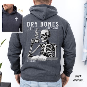 May include: Dark heather gray hoodie with a white cross on the chest. The back features a graphic of a skeleton drinking coffee with the text "DRY BONES COME ALIVE" and "EZEKIEL 37:5".