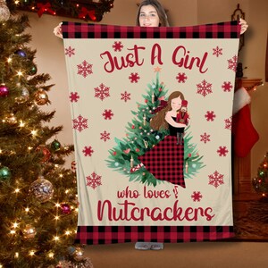 May include: A red and black plaid blanket with a beige background featuring a girl holding a nutcracker in front of a Christmas tree. The text "Just a Girl who loves Nutcrackers" is printed on the blanket.