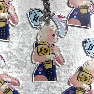 Könnte beinhalten: Schlüsselanhänger mit einer Cartoon-Illustration einer Person mit blonden Haaren, die einen Meisterschaftsgürtel und blaue Shorts mit australischem Flaggenmuster trägt. Jeder Schlüsselanhänger hat einen silbernen Ring und einen Anhänger mit dem Text "THIRD CHANCE".