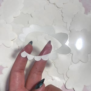 May include: A clear, cloud-shaped sticker with a scalloped edge is held in front of a pile of similar stickers. The sticker is transparent with a white outline. The background is a soft pink.