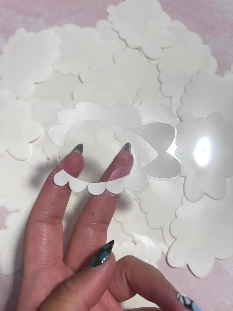 May include: A clear, cloud-shaped sticker with a scalloped edge is held in front of a pile of similar stickers. The sticker is transparent with a white outline. The background is a soft pink.