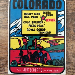 May include: A rectangular sticker featuring a colorful illustration of Colorado with a yellow box listing Rocky Mtn. Nat. Park, Estes Park, Denver, Colo. Springs, Pikes Peak, Royal Gorge, and Trinidad. The text reads Colorado and The Switzerland of America.