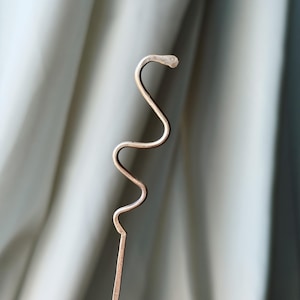 May include: A copper-coloured metal bookmark in the shape of a snake. The bookmark has a slender, wavy body and a detailed head. The design is simple and elegant, ideal for marking pages in books. The bookmark is made of thin wire.