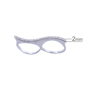 May include: Silver double finger ring with a wave design and a row of clear cubic zirconia stones. The ring is 2 mm wide.