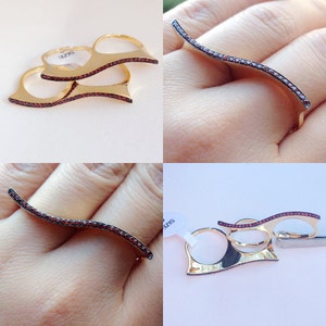 May include: Three gold rings with red stones. The rings are designed to be worn on two fingers. The rings are on a white background.
