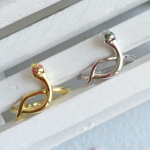 Peut inclure: Deux bagues en forme de serpent, l'une en or avec des yeux roses et l'autre en argent avec des yeux verts.