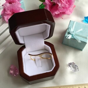 May include: A gold ring with a double band design and a row of small red stones. The ring is displayed in a brown velvet ring box.