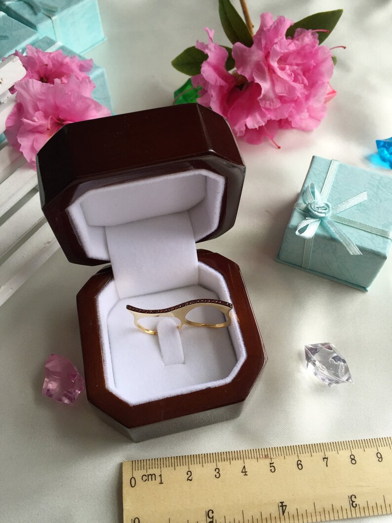 May include: A gold ring with a double band design and a row of small red stones. The ring is displayed in a brown velvet ring box.