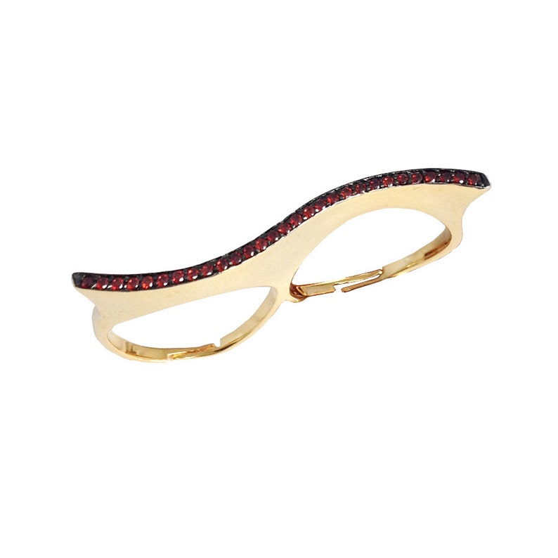 May include: Gold double finger ring with a wave design and red gemstones.