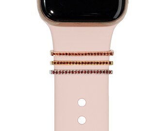 May include: Three watch band charms with a row of small red rhinestones. The charms are in gold, rose gold, and silver.