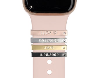 May include: A pink Apple Watch band with four personalized metal charms. The charms are engraved with the words "LUCY ♥", "PATIENCE", "J+B", and "11.26.2002".