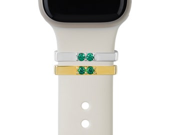 May include: Two watch bands with green gemstones. The top band is silver and the bottom band is gold.