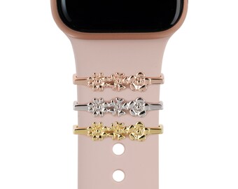 May include: Three Apple Watch bands with floral designs in rose gold, silver, and gold.