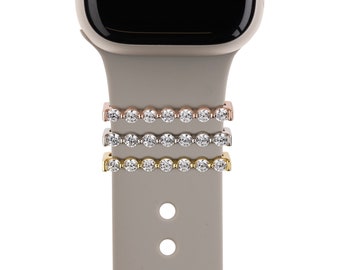 May include: Three Apple Watch band attachments with a row of clear rhinestones. The attachments are in rose gold, silver, and gold.